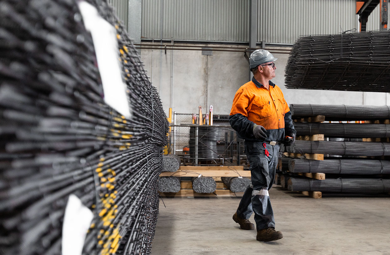 A man in hi vis workwear walking through a warehouse, surrounded by bundles of reinforced steel mesh and rebar